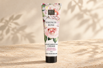 A squeeze tube of B&C French Rose Luxury Hand & Nail Cream stands upright on a textured beige stone surface with soft leaf shadows cast across a warm cream background.